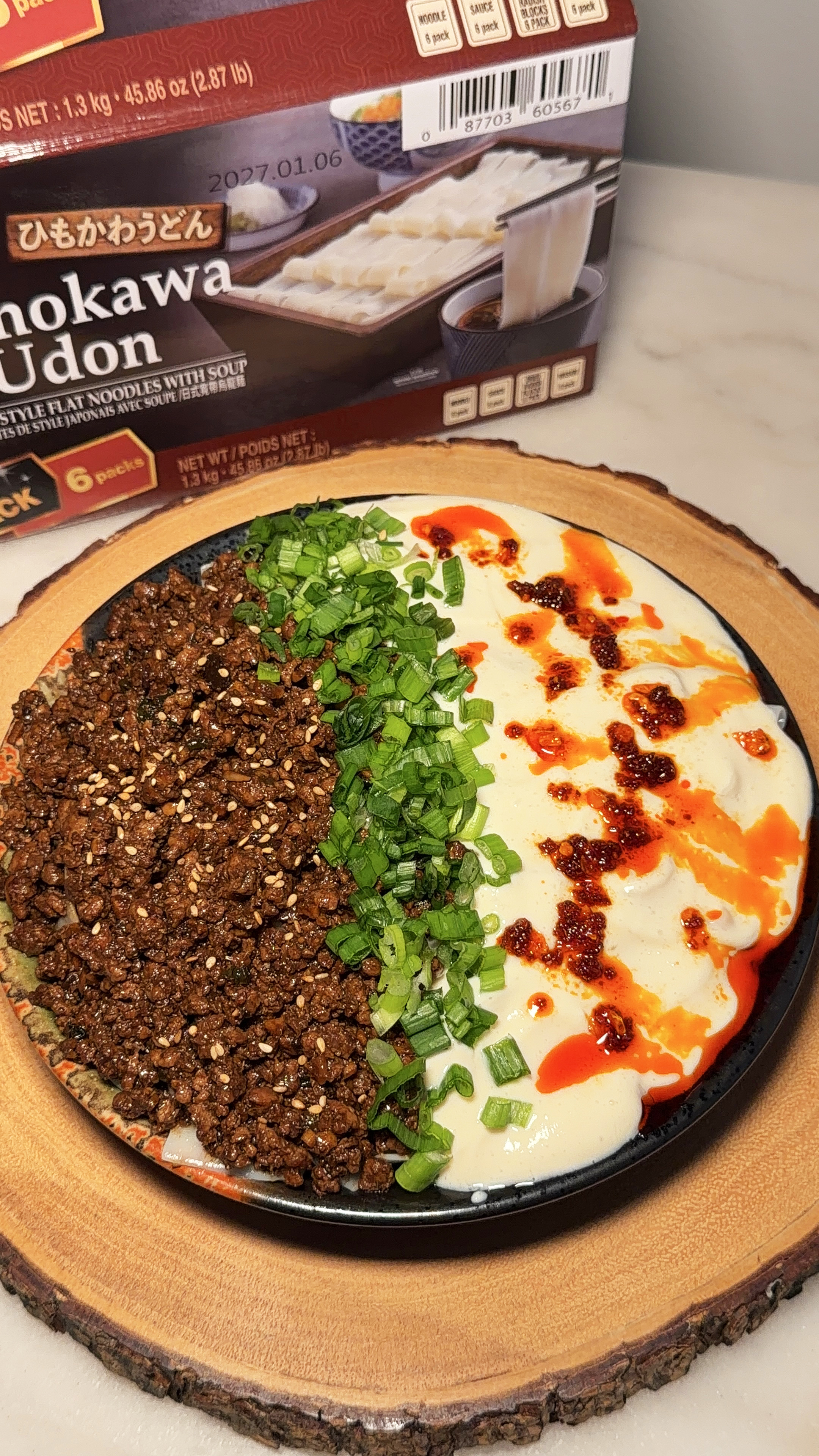 Flat udon noodles topped with spicy ground pork, silken tofu, green onions, sesame seeds, and chili oil